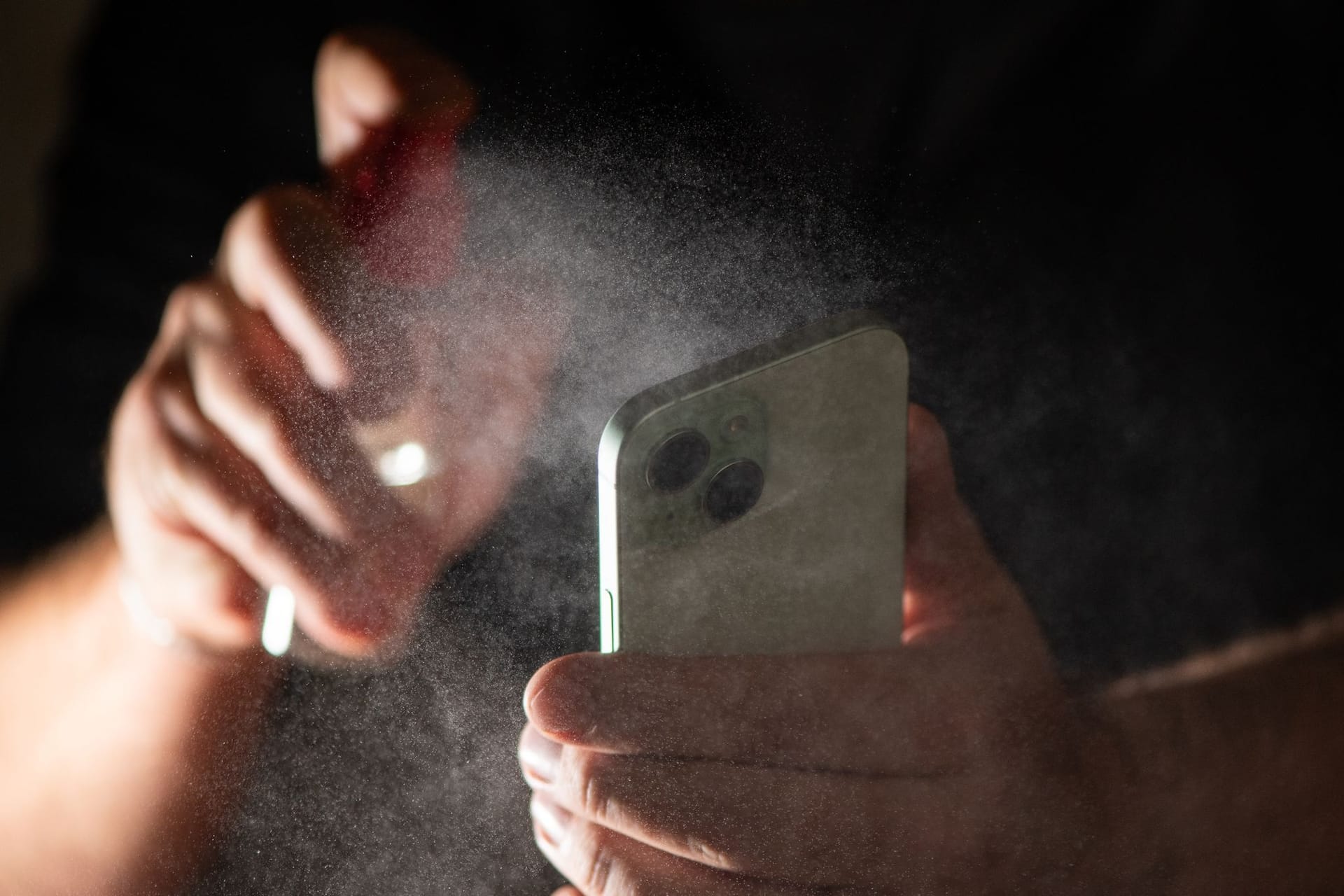 Mann reinigt sein Smartphone mit einem Spray
