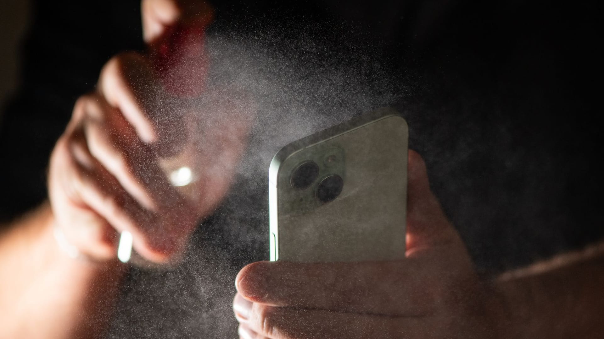 Mann reinigt sein Smartphone mit einem Spray Mann reinigt sein Smartphone mit einem Spray