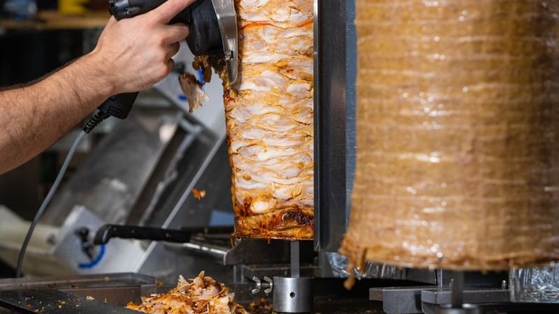 Ein Mitarbeiter einer Dönerbude schneidet Fleisch von einem Dönerspieß. Ein Mitarbeiter einer Dönerbude schneidet Fleisch von einem Dönerspieß.