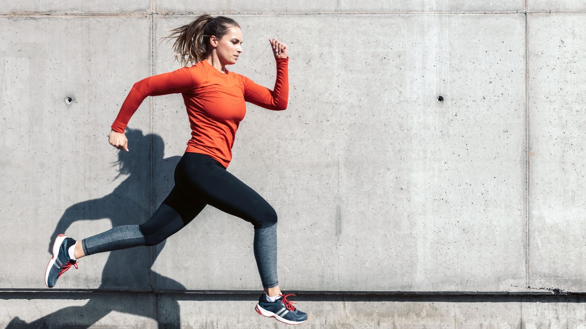 young sportswoman in red sports dress running outdoors in front of concrete wall