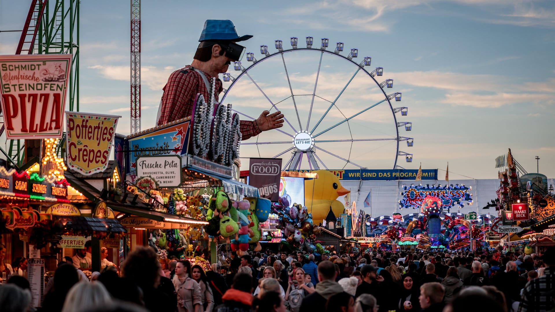 Besucher gehen zwischen Ständen und Fahrgeschäften auf dem 989. Freimarkt in Bremen.