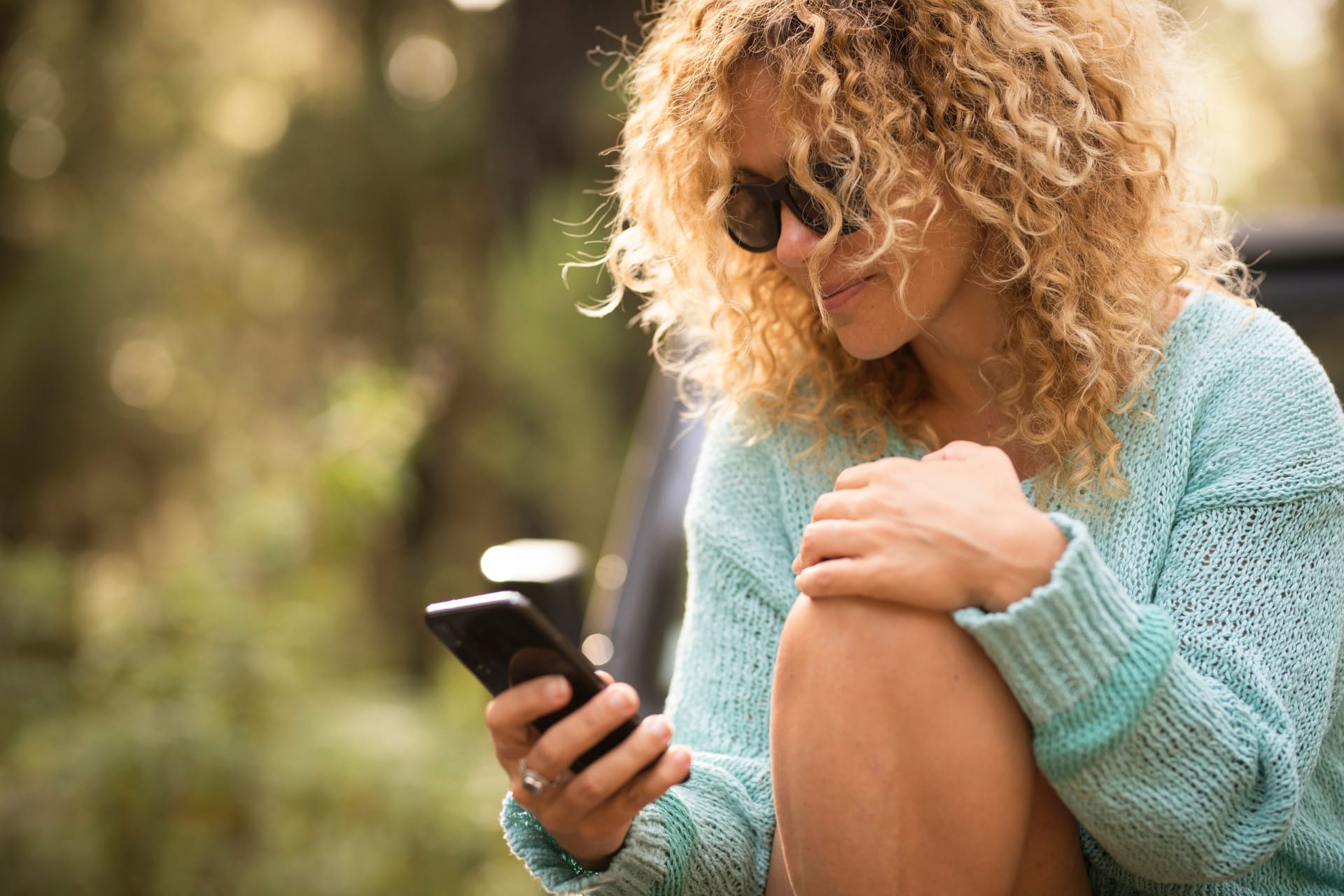 One modern pretty woman using mobile phone outdoor scrolling and writing on app. Outdoor technology leisure activity. Female young people with blonde curly hair searching on cellular. Modern lady outside