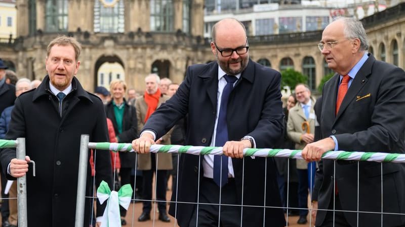 Michael Kretschmer (CDU, l-r), Ministerpräsident von Sachsen, Christian Piwarz (CDU), Finanzminister von Sachsen, und Christian Striefler, Direktor Staatliche Schlösser Burgen und Gärten Sachsen, öffnen bei der offiziellen Übergabe des sanierten Innenhofes des Dresdner Zwingers einen Bauzaun.