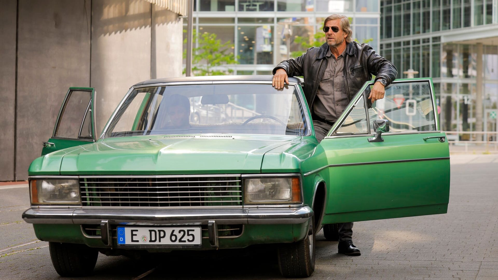 Henning Baum steht an einem grünen Opel Diplomat 5.4: Als Kultkommissar Mick Brisgau ermittelt das Ruhrgebiet-Original ab Ende November wieder bei der Kripo in Essen.