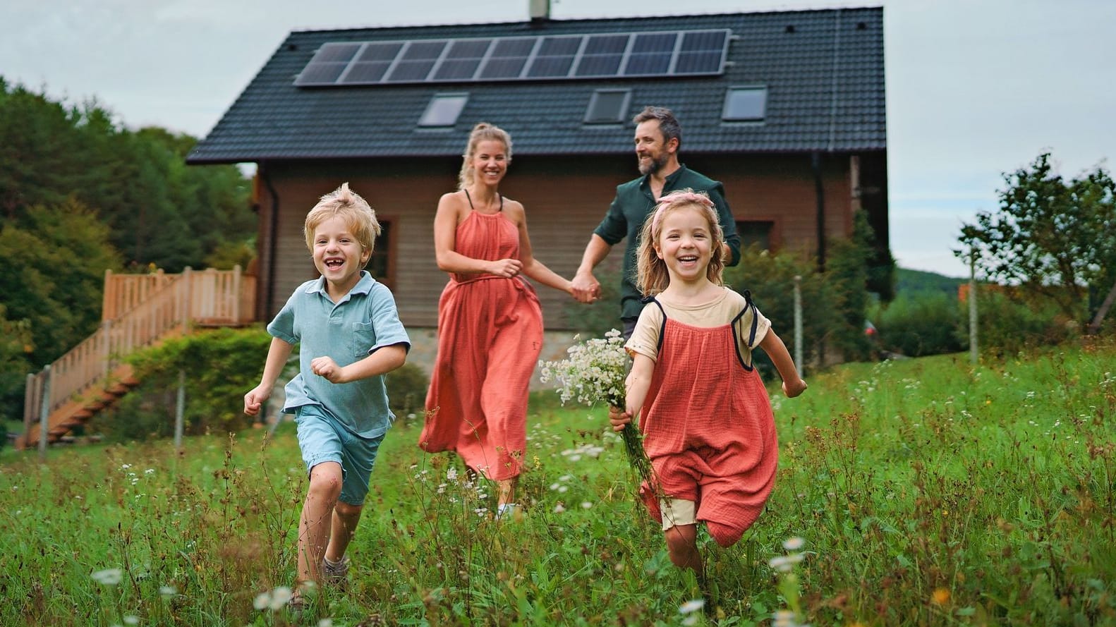 Glückliche Familie auf der Wiese vor dem eigenen Haus im Grünen Glückliche Familie auf der Wiese vor dem eigenen Haus im Grünen