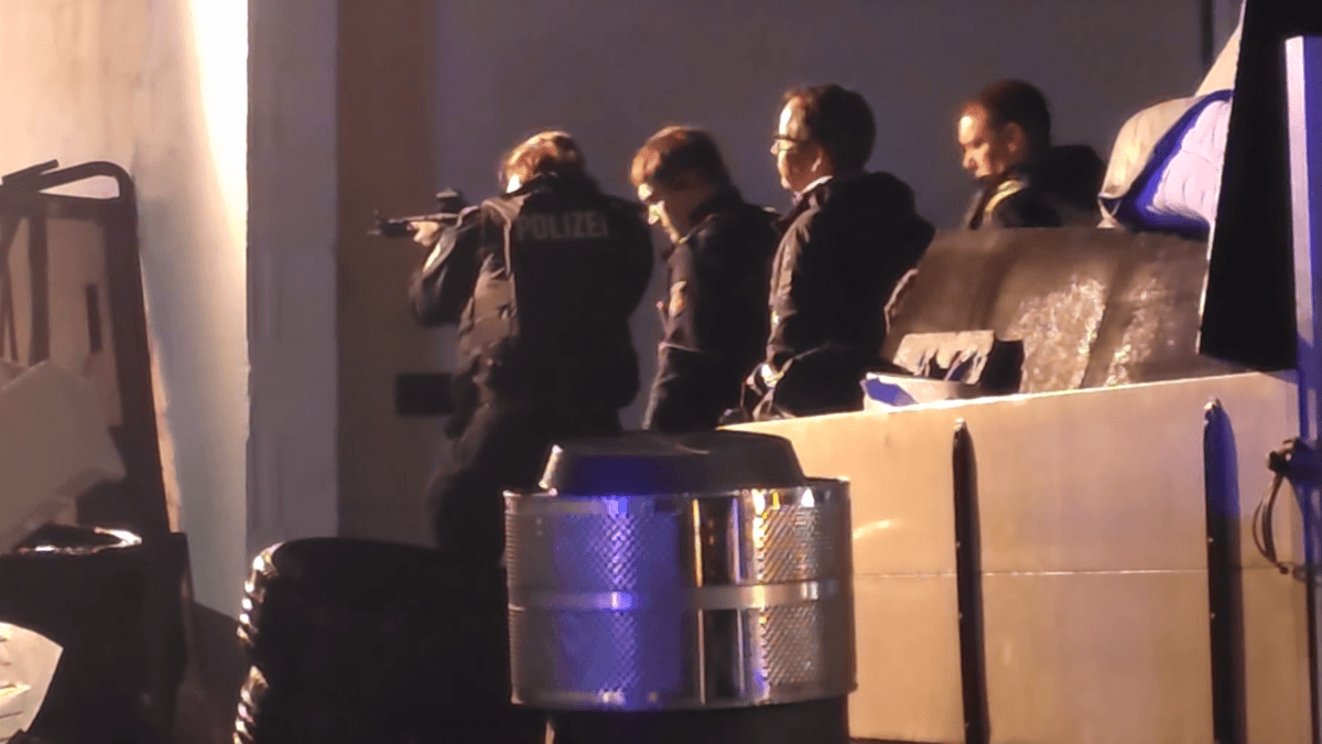 Polizei mit Maschinenpistolen umstellt brennende Halle